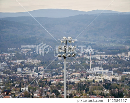 Cityscape features floodlit mountain view. Industrial town below under radiant stadium lamps Cityscape features floodlit mountain view. Industrial town below under radiant stadium lamps 142584537