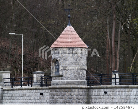 Old fortress with lighting by river. Stone watchtower with lamp post along quiet riverbank scene Old fortress with lighting by river. Stone watchtower with lamp post along quiet riverbank scene 142584673