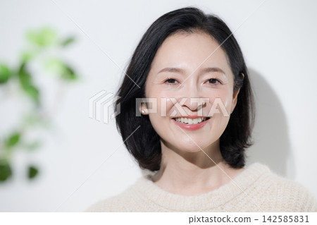 A woman in her 50s smiles naturally, looking directly at the camera against a backdrop of fresh spring greenery, showcasing her radiant and glowing beauty. A woman in her 50s smiles naturally, looking directly at the camera against a backdrop of fresh spring greenery, showcasing her radiant and glowing beauty. 142585831