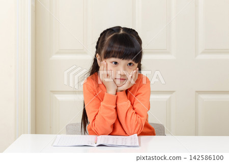 Thoughtful little girl resting her face in hands while staring blanks during study. Thoughtful little girl resting her face in hands while staring blanks during study. 142586100