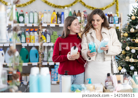 Woman with daughter choosing shampoo in festively decorated store Woman with daughter choosing shampoo in festively decorated store 142586515