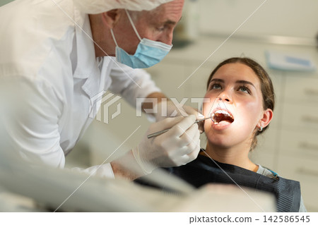 Mature man doctor dentist in white coat examines oral cavity of girl patient in dentistry. Mature man doctor dentist in white coat examines oral cavity of girl patient in dentistry. 142586545
