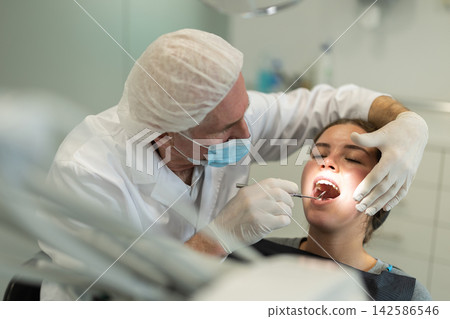 Mature man doctor dentist in white coat examines oral cavity of girl patient in dentistry. Mature man doctor dentist in white coat examines oral cavity of girl patient in dentistry. 142586546