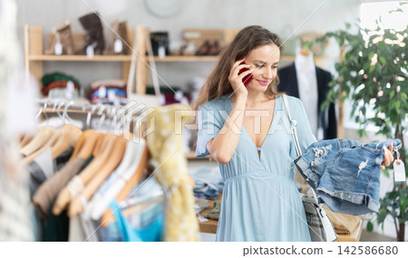 woman in a summer dress chooses jeans and calls on her cell phone woman in a summer dress chooses jeans and calls on her cell phone 142586680