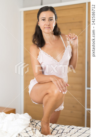 Woman posing in nightgown lying on bed in bedroom Woman posing in nightgown lying on bed in bedroom 142586712