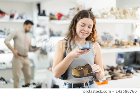 While shopping and choosing shoes, woman scans QR code on sandals product While shopping and choosing shoes, woman scans QR code on sandals product 142586760