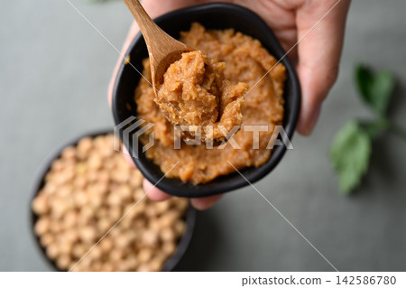 miso paste in a black bowl with spoon holding by hand miso paste in a black bowl with spoon holding by hand 142586780