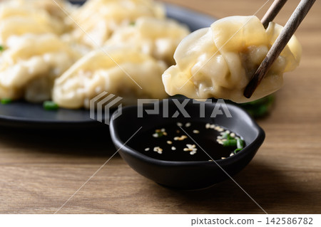 Dumpling stuffed with minced pork held by chopsticks eaten with sesame oil dipping sauce, Asian food Dumpling stuffed with minced pork held by chopsticks eaten with sesame oil dipping sauce, Asian food 142586782