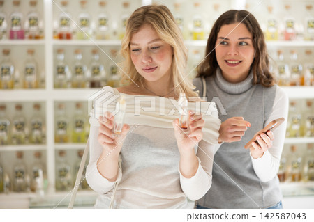 Girl shows phone screen to her female friend in perfume store Girl shows phone screen to her female friend in perfume store 142587043