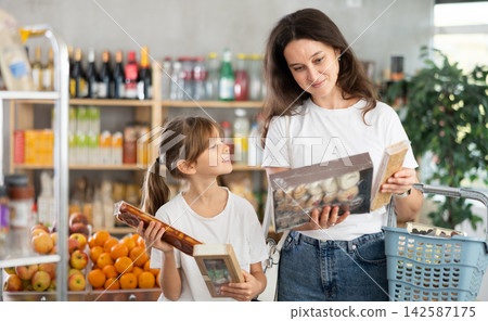 Mother consults with her daughter about which sweets to buy in the grocery section of supermarket - nougat or cookies Mother consults with her daughter about which sweets to buy in the grocery section of supermarket - nougat or cookies 142587175
