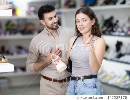 Young woman choosing sandals, her male partner helps at shoe store 142587176