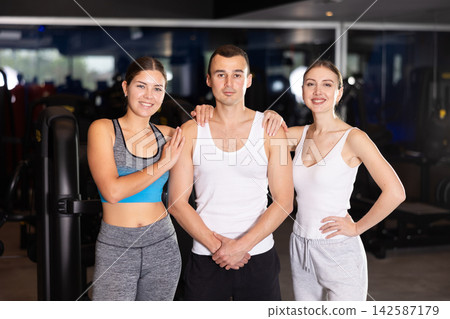 Positive young man and two girls posing together in gym 142587179