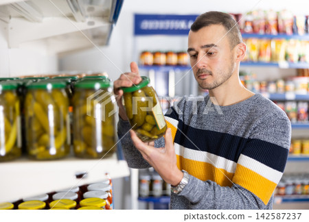 Adult man chooses pickled cucumbers in store Adult man chooses pickled cucumbers in store 142587237