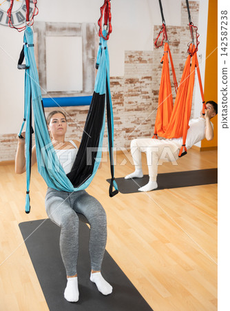 Girl doing aerial pilates exercises with suspended hammock in studio 142587238
