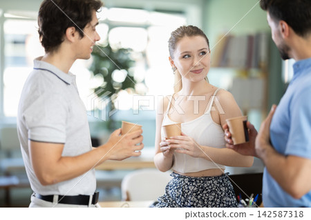 Two male and girl colleagues drink coffee and have nice conversation during break Two male and girl colleagues drink coffee and have nice conversation during break 142587318