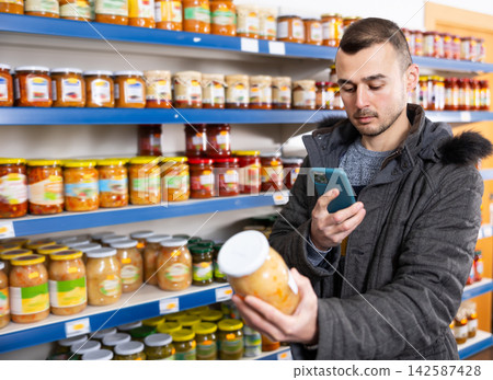Man scans barcode on jar of sauerkraut using a smartphone while shopping in grocery store Man scans barcode on jar of sauerkraut using a smartphone while shopping in grocery store 142587428