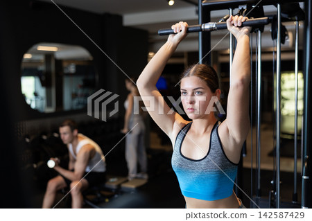 Sportive young girl training on cable exercise machine in gym Sportive young girl training on cable exercise machine in gym 142587429