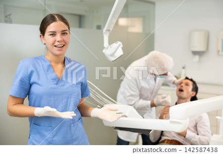 Young woman nurse in blue suit is standing in dental office, clinic Young woman nurse in blue suit is standing in dental office, clinic 142587438