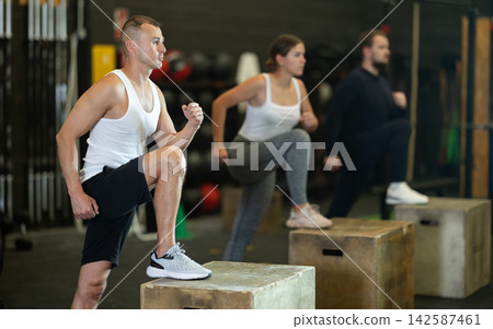 Sportive young guy doing step-up exercises with box during crossfit workout Sportive young guy doing step-up exercises with box during crossfit workout 142587461