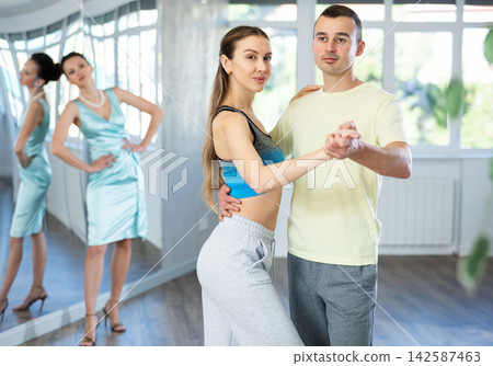 Couple in comfortable sports clothes waltz dancing during individual lesson Couple in comfortable sports clothes waltz dancing during individual lesson 142587463