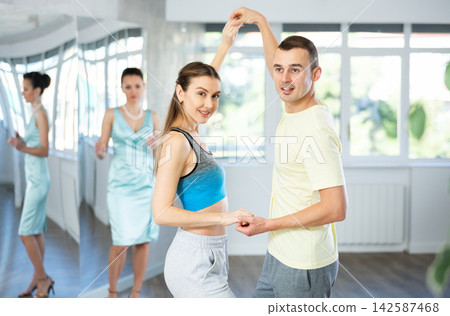 Couple in comfortable sports clothes waltz dancing during individual lesson Couple in comfortable sports clothes waltz dancing during individual lesson 142587468