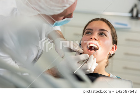 Mature man doctor dentist in white coat examines oral cavity of girl patient in dentistry. Mature man doctor dentist in white coat examines oral cavity of girl patient in dentistry. 142587648
