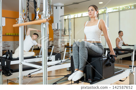 Girl performing pulling straps exercise on Pilates reformer with box Girl performing pulling straps exercise on Pilates reformer with box 142587652