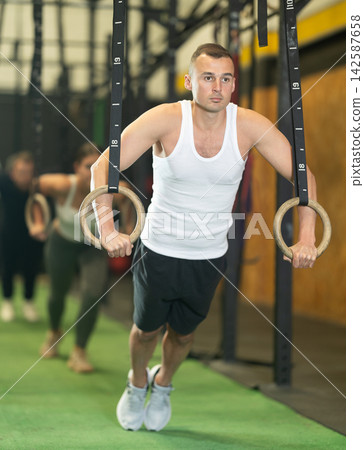 Man performing chest push-ups with gymnastic rings during workout in gym Man performing chest push-ups with gymnastic rings during workout in gym 142587658