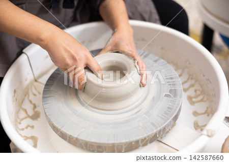 Woman potter works with potter weel, craftsman hands close up. Hands of potter making clay pot Woman potter works with potter weel, craftsman hands close up. Hands of potter making clay pot 142587660
