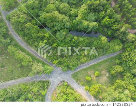 Aerial top down view of rural road intersection beside a freshwater pond and dense tropical forest. Green infrastructure, natural habitat and sustainable countryside landscape. Freshwater ecosystem. Aerial top down view of rural road intersection beside a freshwater pond and dense tropical forest. Green infrastructure, natural habitat and sustainable countryside landscape. Freshwater ecosystem. 142588534