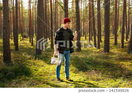 Man foraging and mushroom picking in a sunlit forest during the autumn harvest, collecting wild food in a basket. Man foraging and mushroom picking in a sunlit forest during the autumn harvest, collecting wild food in a basket. 142589826