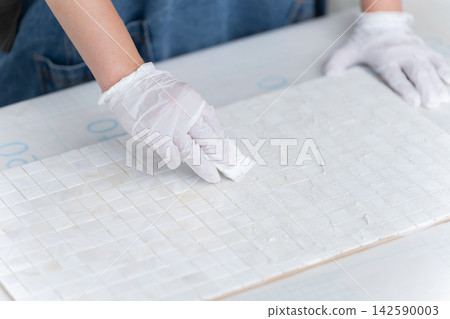 A woman filling in the grout between tiles with putty - DIY A woman filling in the grout between tiles with putty - DIY 142590003