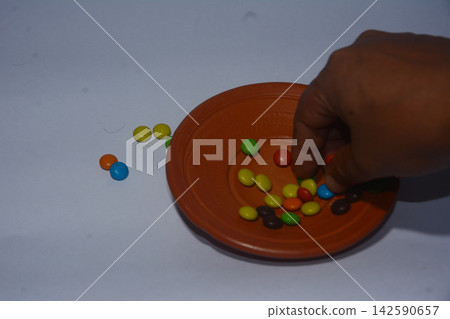 Person picking colorful chocolate candies from a small clay bowl Person picking colorful chocolate candies from a small clay bowl 142590657