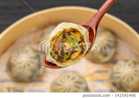 close-up of a steamed vegetarian bun on a wooden spoon, showing the rich vegetable and mushroom filling. close-up of a steamed vegetarian bun on a wooden spoon, showing the rich vegetable and mushroom filling. 142591498