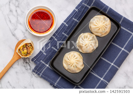 freshly steamed healthy vegetarian buns arranged on a modern black plate over a marble tabletop. freshly steamed healthy vegetarian buns arranged on a modern black plate over a marble tabletop. 142591503