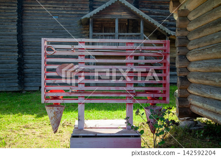Outdoor fire safety board with buckets, axe, hook, and fire extinguisher near wooden village houses Outdoor fire safety board with buckets, axe, hook, and fire extinguisher near wooden village houses 142592204