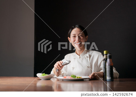 一位微笑的女廚師正在烹飪。 142592674