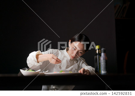 一位女廚師正在往菜餚上撒鹽。 一位女廚師正在往菜餚上撒鹽。 142592831