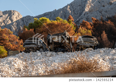 Burned out cars in rocky Croatian landscape beneath autumn mountain slopes Burned out cars in rocky Croatian landscape beneath autumn mountain slopes 142593214