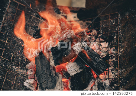 Close-up of burning charcoal with bright orange flames in a barbecue grill. Close-up of burning charcoal with bright orange flames in a barbecue grill. 142593275