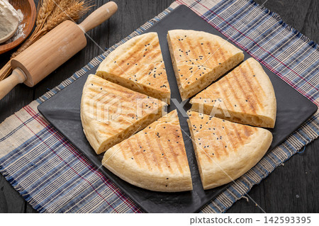 authentic Xinyang thick flatbread with a cut slice, crispy grilled Chinese wheat bread on a black platter. authentic Xinyang thick flatbread with a cut slice, crispy grilled Chinese wheat bread on a black platter. 142593395