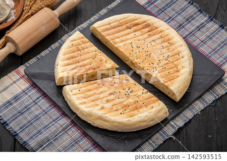 authentic Xinyang thick flatbread with a cut slice, crispy grilled Chinese wheat bread on a black platter. authentic Xinyang thick flatbread with a cut slice, crispy grilled Chinese wheat bread on a black platter. 142593515