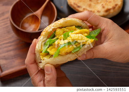 hands holding Chinese sesame flatbread sandwich stuffed with scrambled eggs and green peppers 142593551