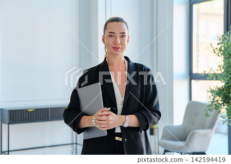 Confident businesswoman holding laptop standing in modern office portrait Confident businesswoman holding laptop standing in modern office portrait 142594419