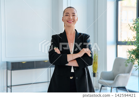 Confident businesswoman standing with arms crossed in modern office portrait 142594421