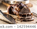 Juicy roasted pork shoulder with a crispy crust is sliced on a wooden board next to a sharp knife. This delicious meat dish looks very appetizing and is an ideal choice for a traditional family 142594446
