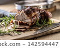 Tasty roasted pork neck with a crispy crust is garnished with fresh rosemary and sliced on a wooden board. This professional culinary shot will fit perfectly in cookbooks, restaurant menus, or food 142594447
