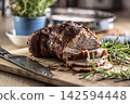 Tasty roasted pork neck with a crispy crust is garnished with fresh rosemary and sliced on a wooden board. This professional culinary shot will fit perfectly in cookbooks, restaurant menus, or food 142594448