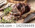 Tasty roasted pork neck with a crispy crust is garnished with fresh rosemary and sliced on a wooden board. This professional culinary shot will fit perfectly in cookbooks, restaurant menus, or food 142594449