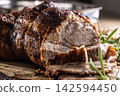 Detailed macro shot of juicy roasted pork shoulder with a perfectly browned crust. Tender meat slices lie on a wooden board next to fragrant rosemary, creating an inviting composition for any gourmet 142594450
